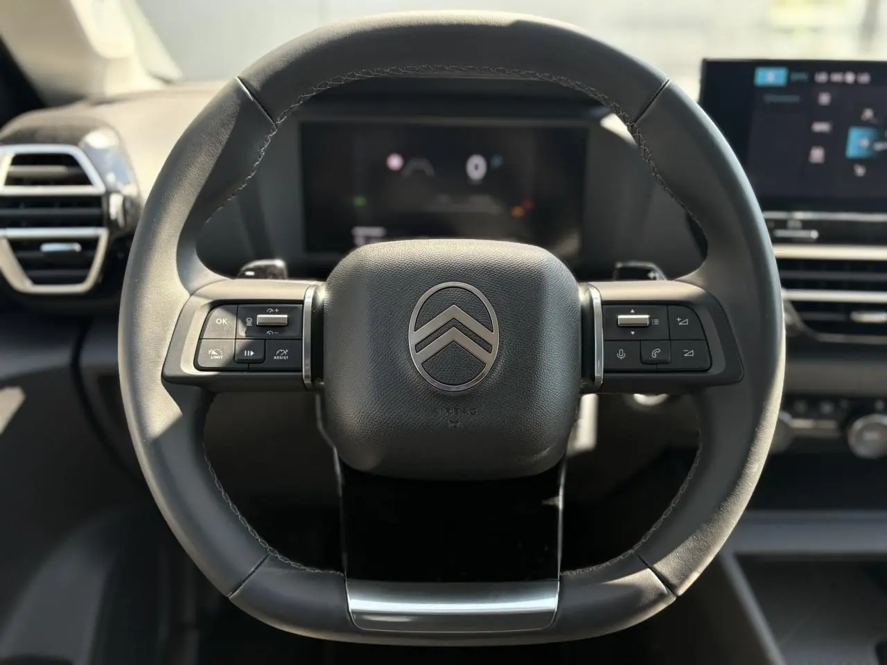 Vue rapprochée du volant cuir noir de la Citroën C4 Hybrid 2025 avec commandes intégrées et tableau de bord numérique flou.