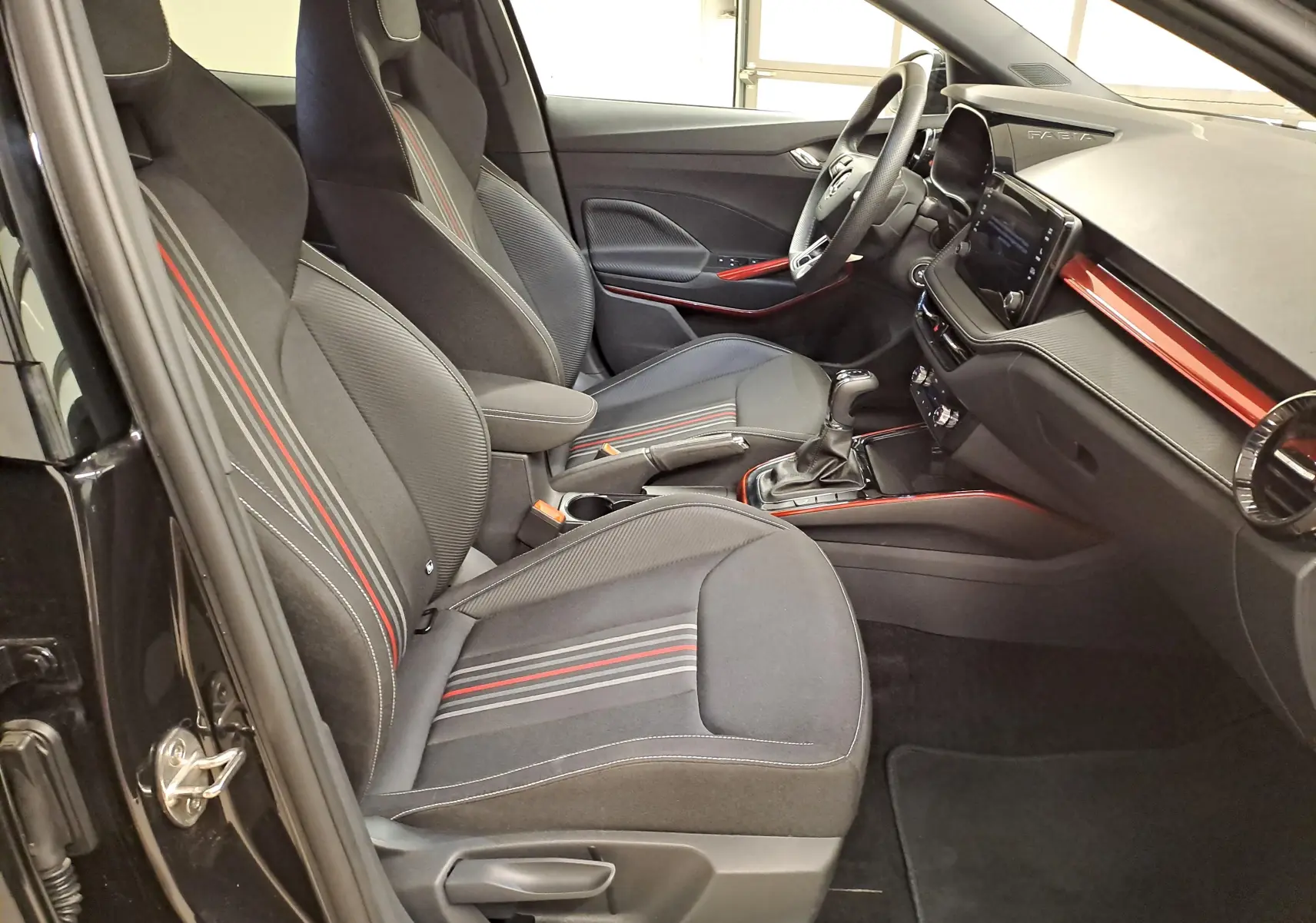 Vue intérieure côté conducteur de la Skoda Fabia 2024 noire avec sièges sport et détails rouges sur tableau de bord et console.