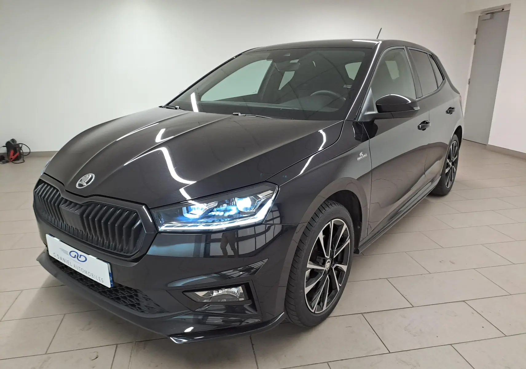 Vue 3/4 avant d'une Skoda Fabia 2024 noire Magic Nacré avec phares allumés et jantes sportives noires et argentées.