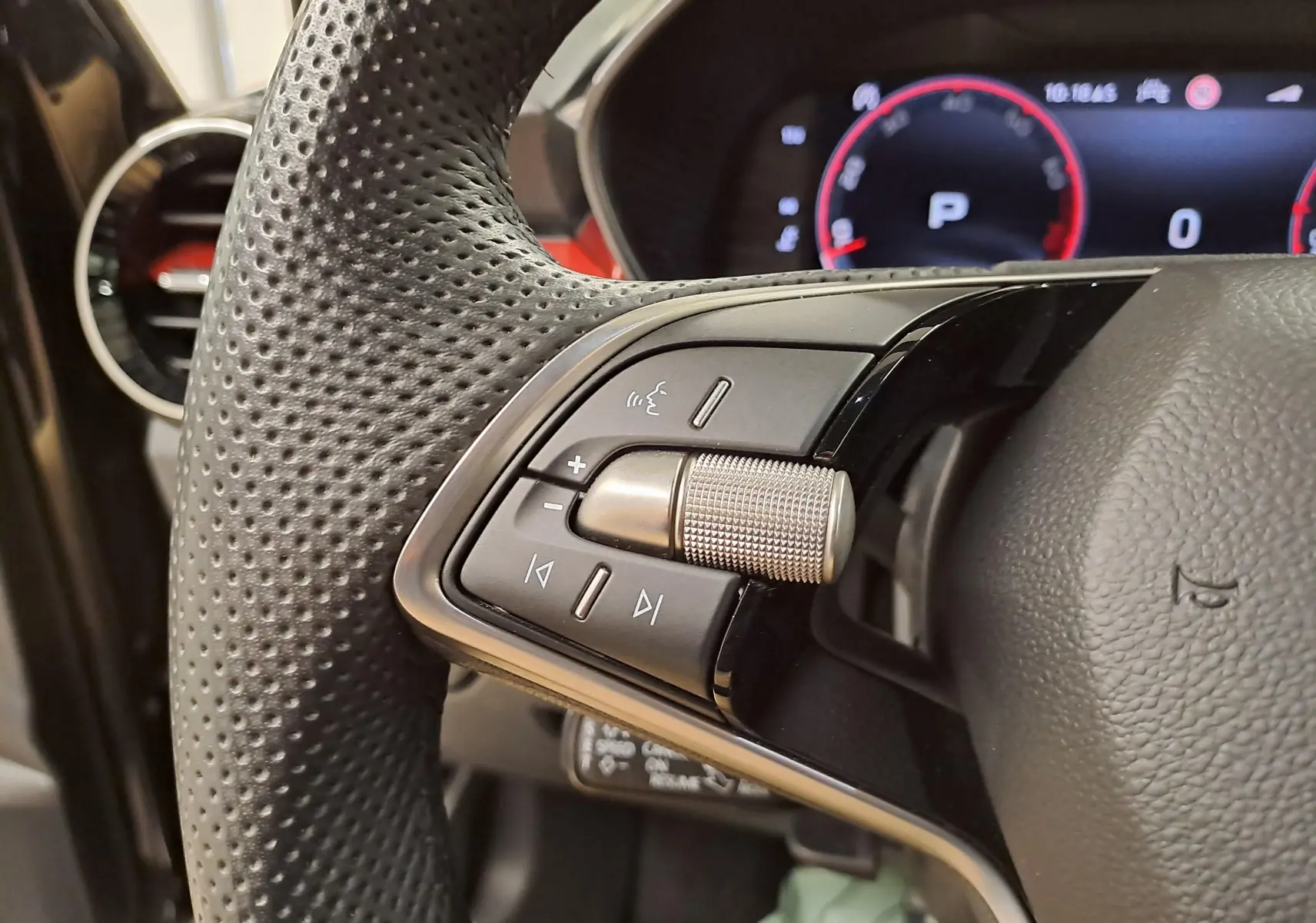 Gros plan sur les commandes gauche du volant perforé d'une Skoda Fabia 1.5 TSI 2024 avec tableau de bord numérique en arrière-plan.