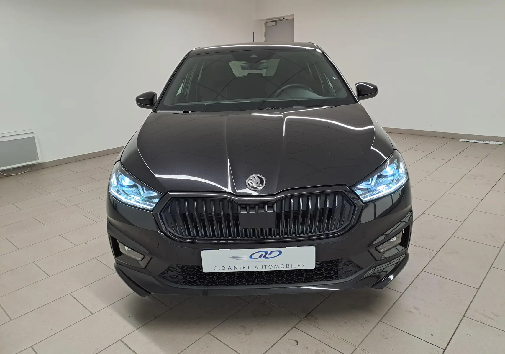 Vue frontale d'une Skoda Fabia 1.5 TSI 150 DSG7 Monte-Carlo en Noir Magic Nacré avec phares LED allumés.