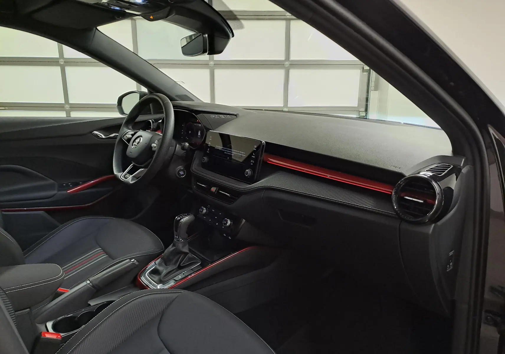 Intérieur avant droit de la Skoda Fabia 2024 noir Magic Nacré, avec tableau de bord noir et éclairage d'ambiance rouge.