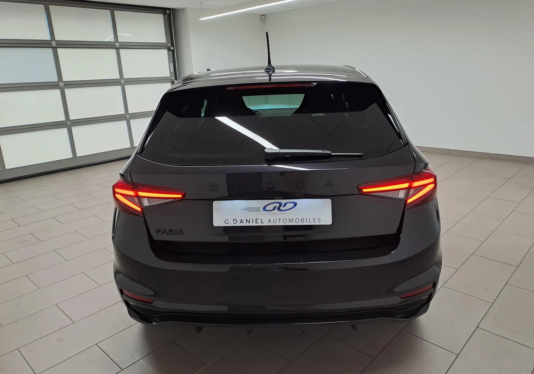 Vue arrière d'une Skoda Fabia 2024 noire Magic Nacré avec feux LED allumés dans un garage lumineux.