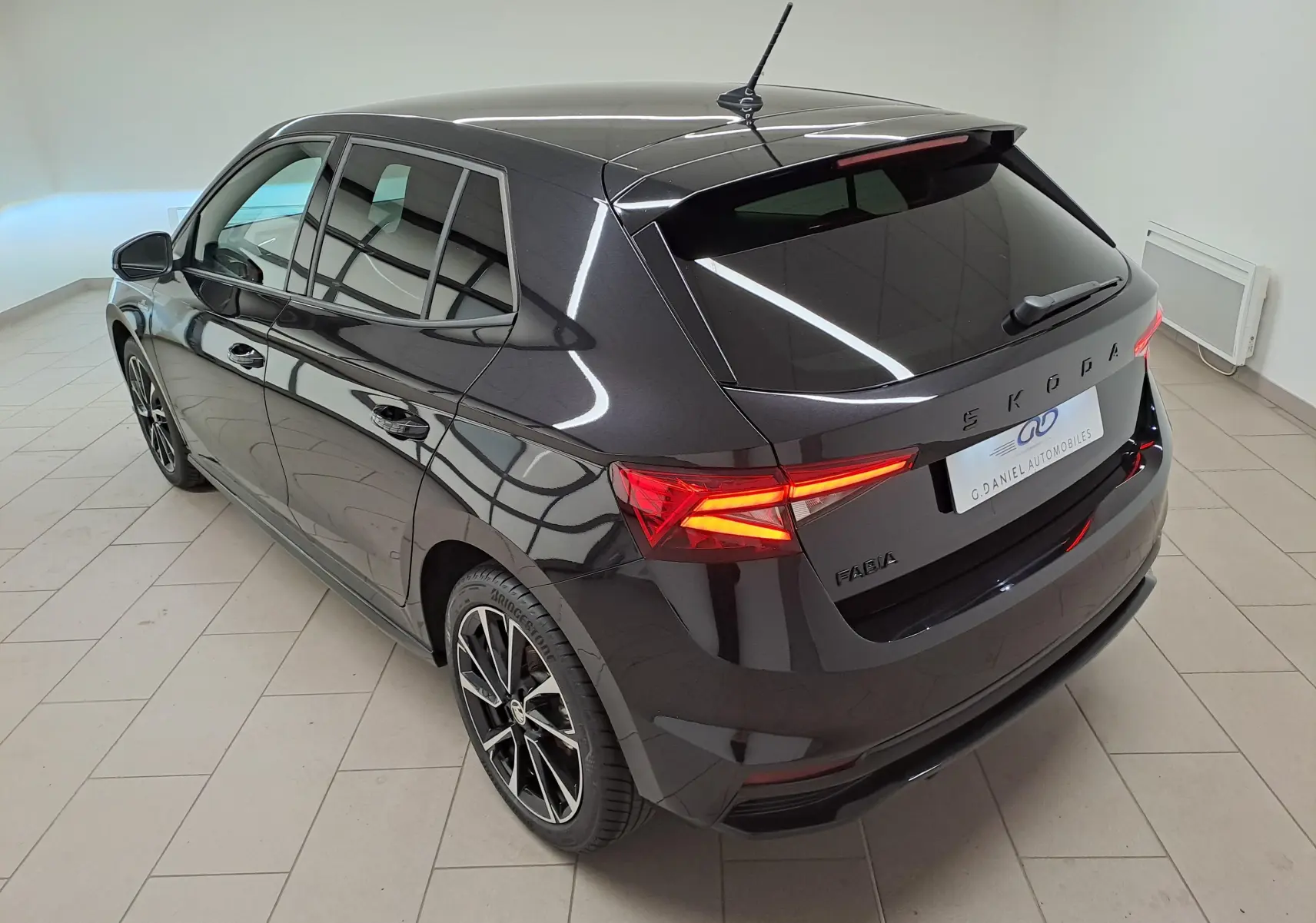 Vue 3/4 arrière gauche d'une Skoda Fabia 2024 noire Magic Nacré avec feux arrière allumés et jantes alliage noires.