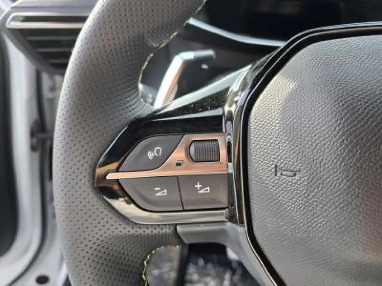 Gros plan sur le volant cuir noir avec logo Peugeot et badge GT du Peugeot 2008 hybride blanc, intérieur moderne.