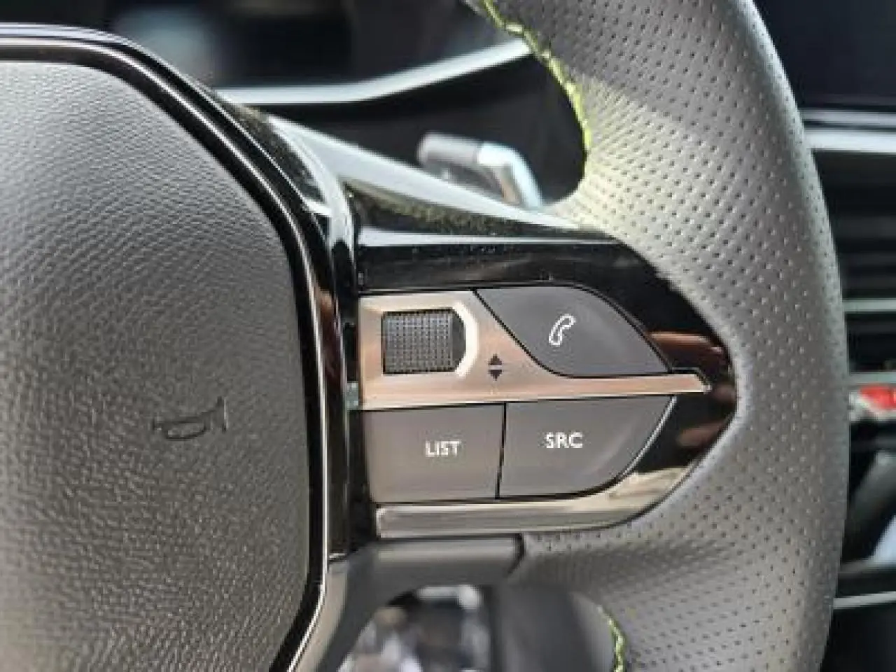 Gros plan sur les commandes gauche du volant cuir perforé de la Peugeot 2008 blanche toit noir, version hybride 2025.