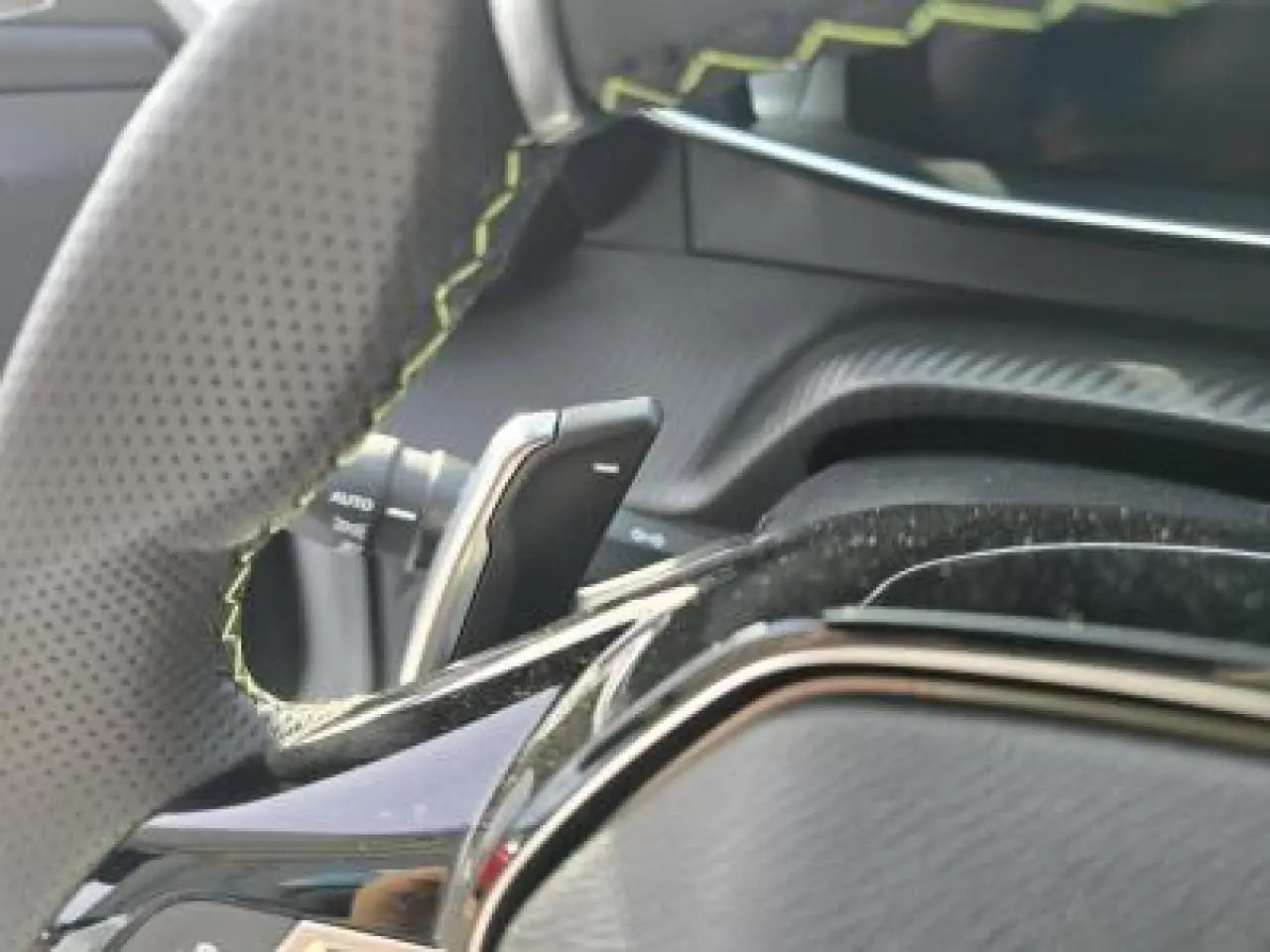 Gros plan sur les commandes gauche du volant cuir perforé du Peugeot 2008 blanc Okenite, version hybride 2025.