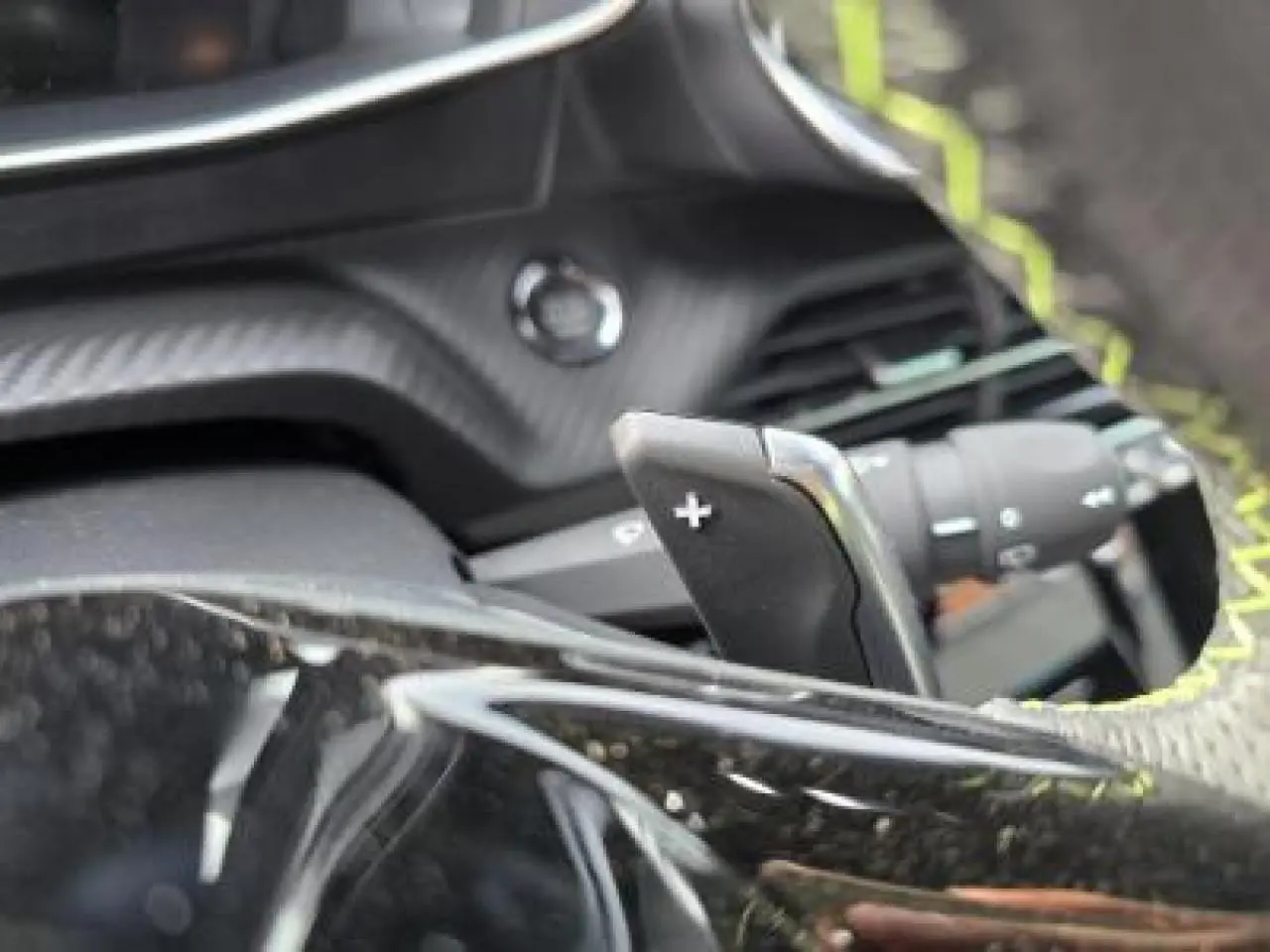 Gros plan sur le volant cuir perforé avec surpiqûres vertes et palettes de changement de vitesse du Peugeot 2008 hybride 2025.