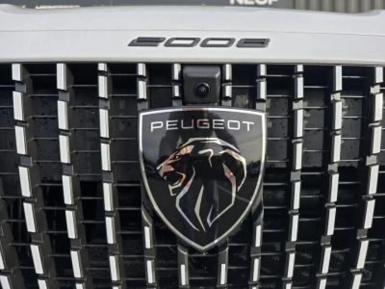 Peugeot 2008 hybride 2025 blanc Okenite toit noir en vue 3/4 arrière côté gauche avec barres de toit noires.