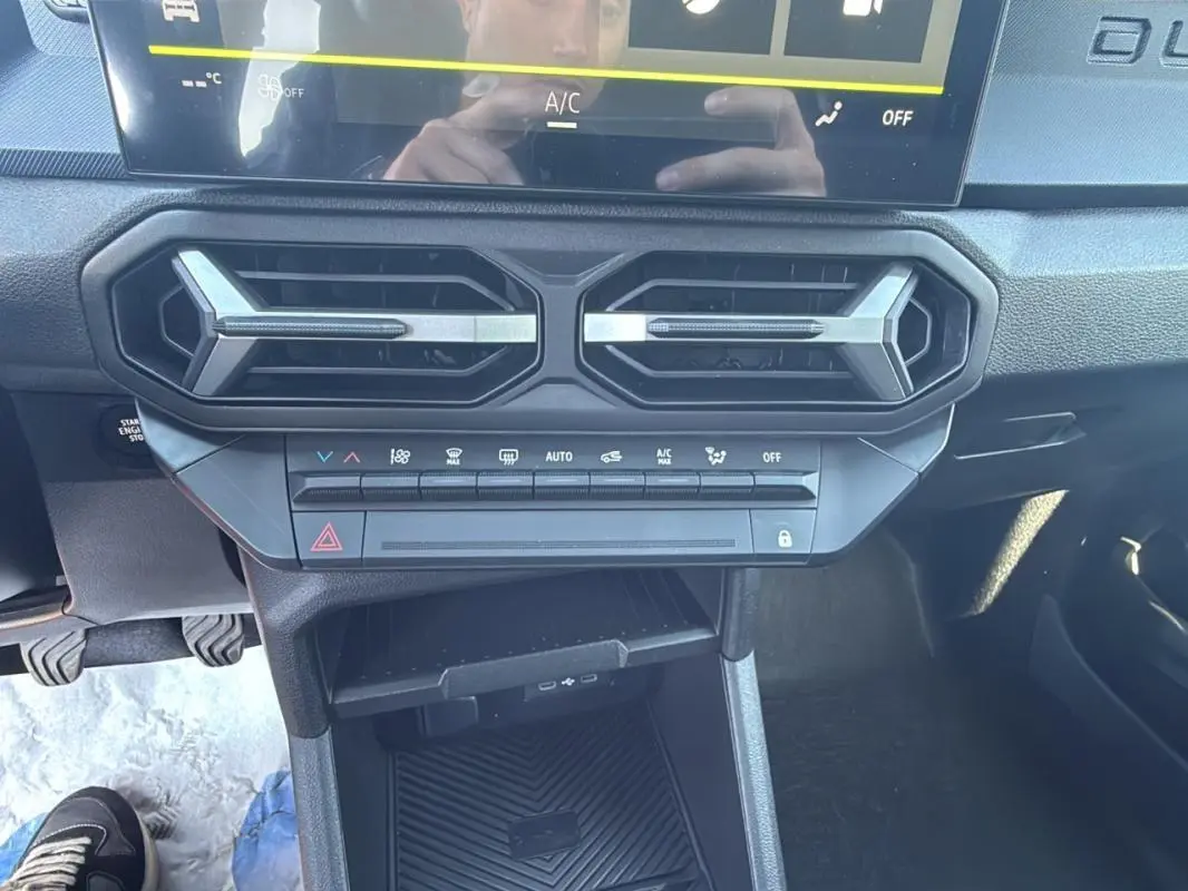 Détail du tableau de bord du Dacia Duster 2025 avec commandes climatisation et aérateurs hexagonaux noirs.