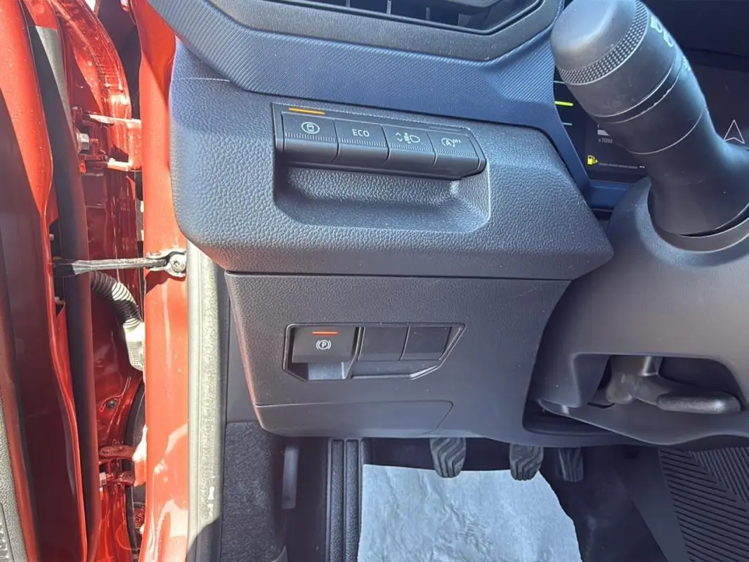 Vue intérieure côté gauche du tableau de bord du Dacia Duster orange 2025 avec commandes d'assistance et pédales visibles.