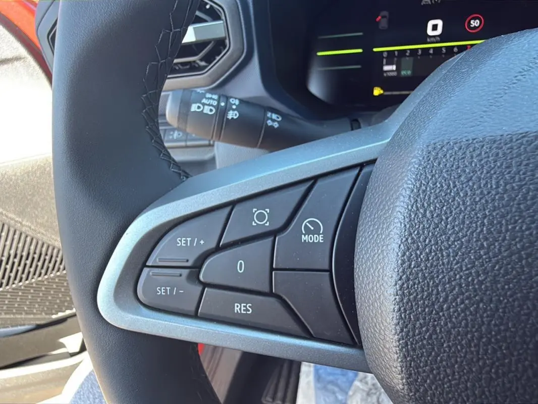 Gros plan sur les commandes du régulateur de vitesse au volant du Dacia Duster orange 2025 côté gauche.