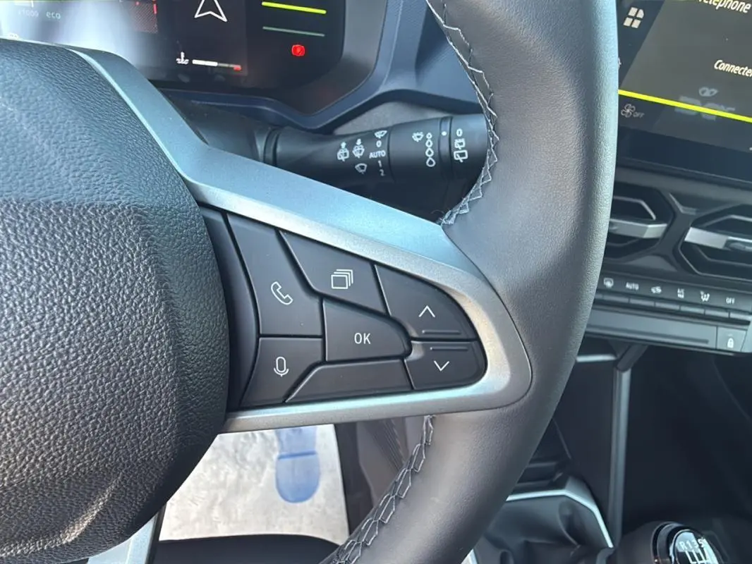 Gros plan sur le volant du Dacia Duster 2025 orange, montrant les commandes multifonctions côté gauche et partie du tableau de bord.