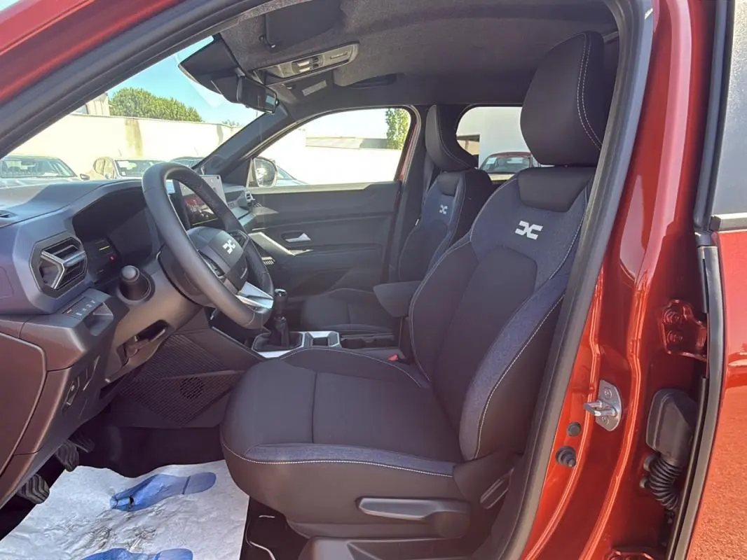 Vue intérieure côté conducteur du Dacia Duster orange 2025, montrant les sièges et le volant réglable.