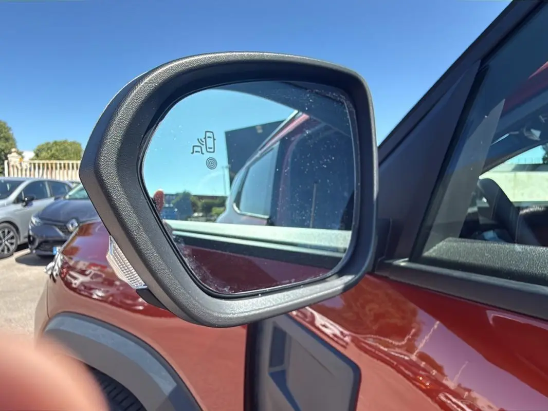 Gros plan sur le rétroviseur côté gauche du Dacia Duster orange 2025, avec capteur d'angle mort visible.