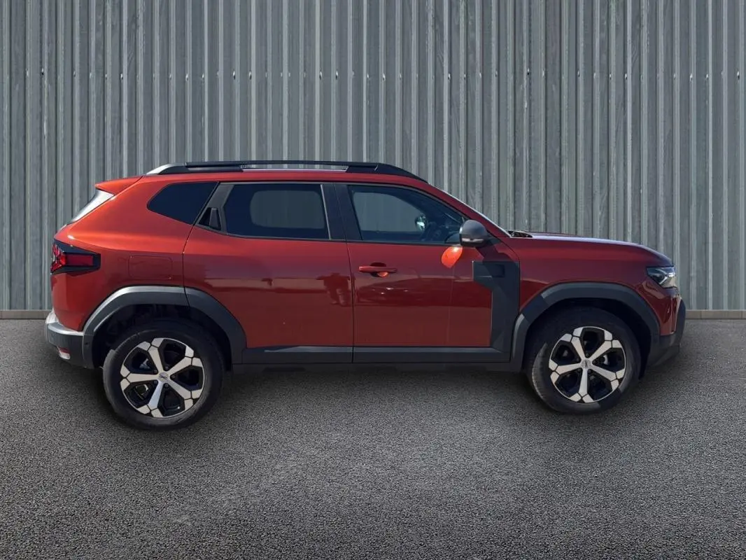 Profil côté gauche d'un Dacia Duster orange 2025 avec barres de toit et jantes alliage 18 pouces.