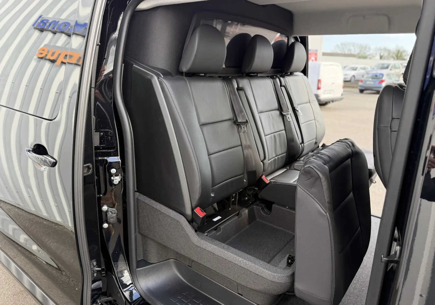 Vue latérale intérieure du Citroën Jumpy noir Perla montrant la banquette arrière en cuir avec siège rabattable.