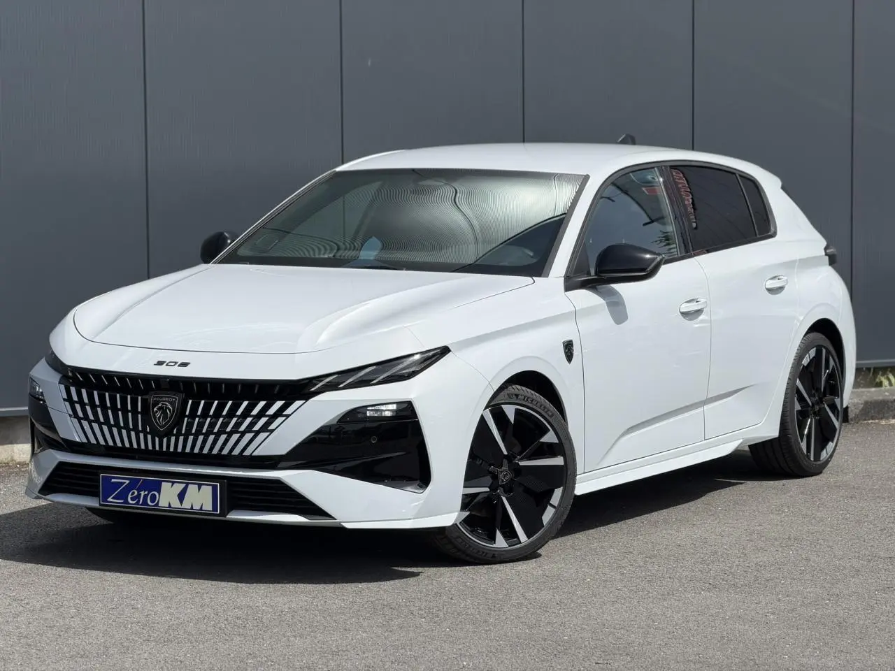Peugeot 308 NV Hybrid blanc Okenite vue 3/4 avant droit avec jantes bi-tons et calandre distinctive noire.