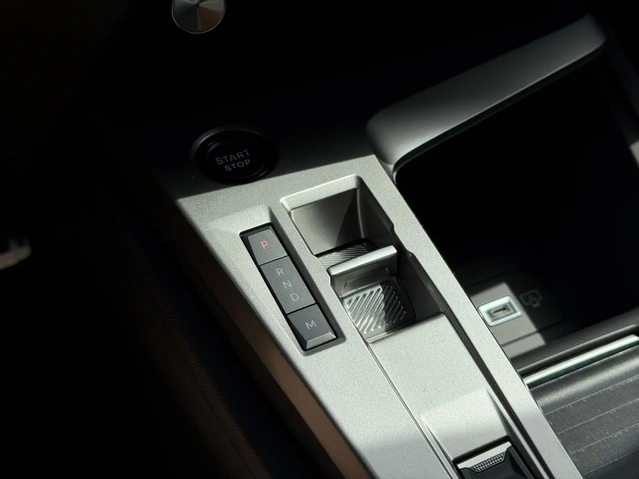 Gros plan sur la console centrale argentée de la Peugeot 308 NV Hybrid 145 GT avec commandes de boîte auto et bouton start/stop.