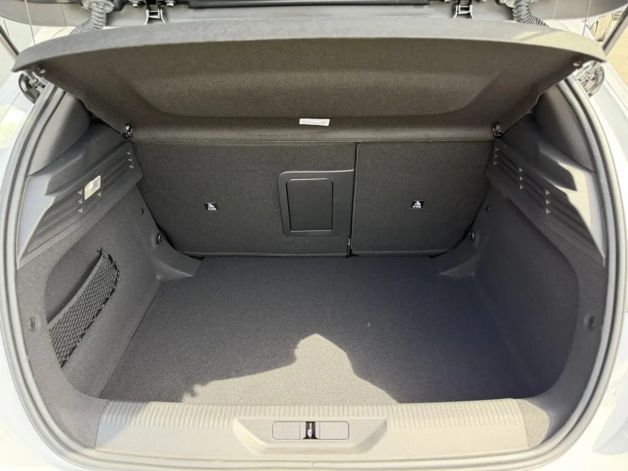Coffre ouvert vu de l'arrière d'une Peugeot 308 blanc Okenite, avec banquette arrière rabattable et filet de rangement latéral.