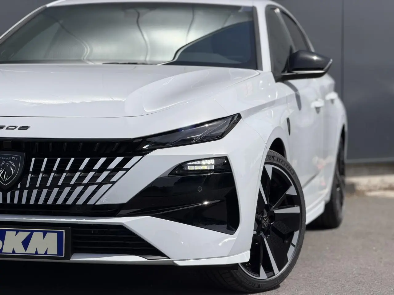Vue avant droite d'une Peugeot 308 blanche Okenite avec calandre noire et jantes alliage 18" bi-tons.