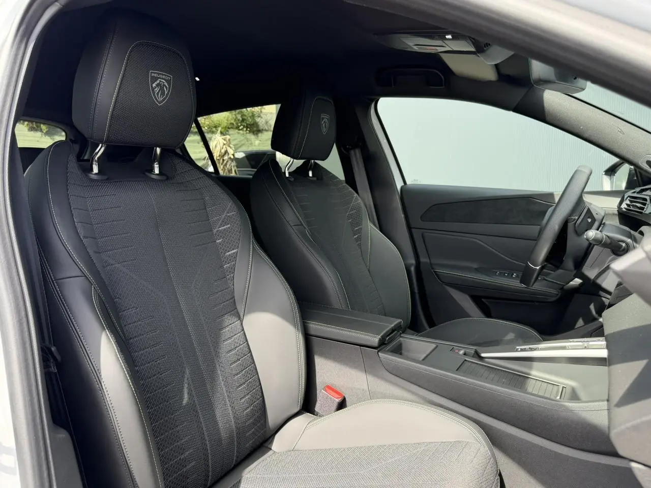 Vue intérieure côté conducteur de la Peugeot 308 NV Hybrid 145 GT avec sièges noirs embossés et volant cuir.