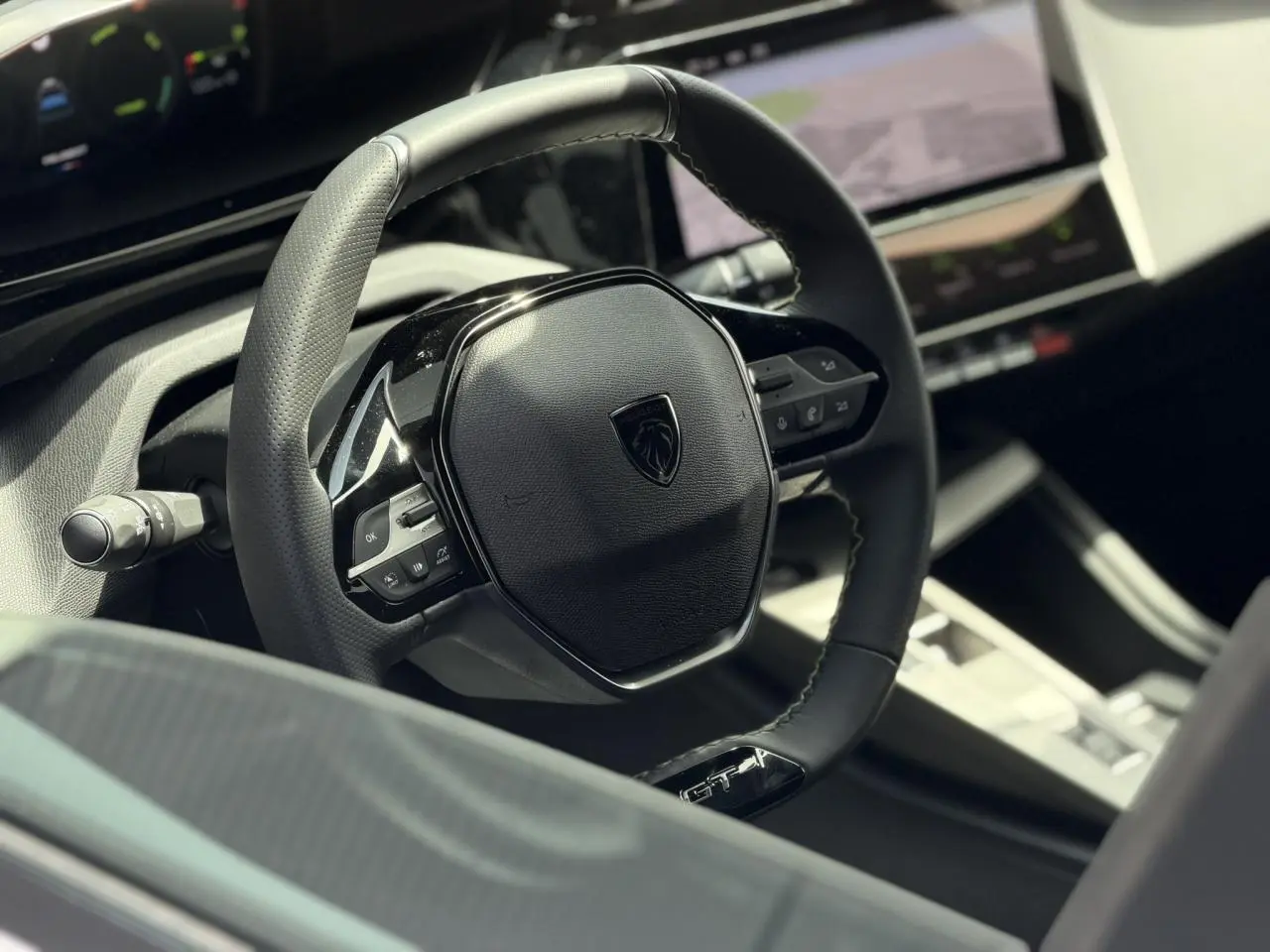 Vue rapprochée du volant cuir noir GT du Peugeot 308 NV Hybrid 145 GT avec tableau de bord numérique et écran tactile.