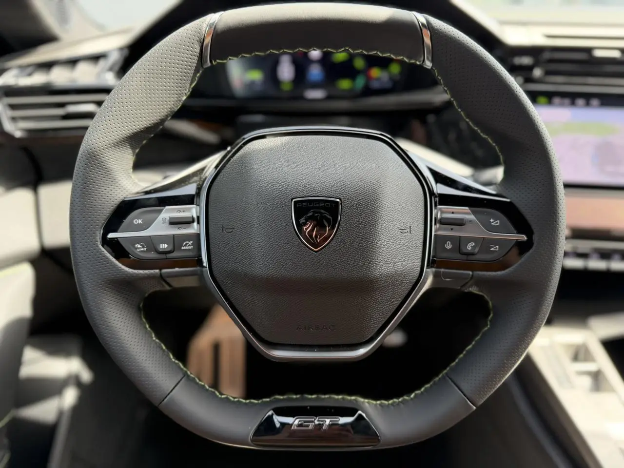 Gros plan sur le volant compact GT en cuir noir avec surpiqûres vert Adamite et logo Peugeot central.