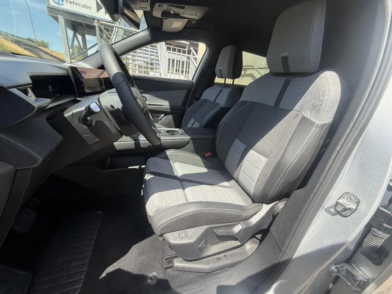 Vue intérieure côté conducteur de l’Opel Grandland gris kristall 2025, mettant en valeur les sièges tissu bicolores et le tableau de bord moderne.