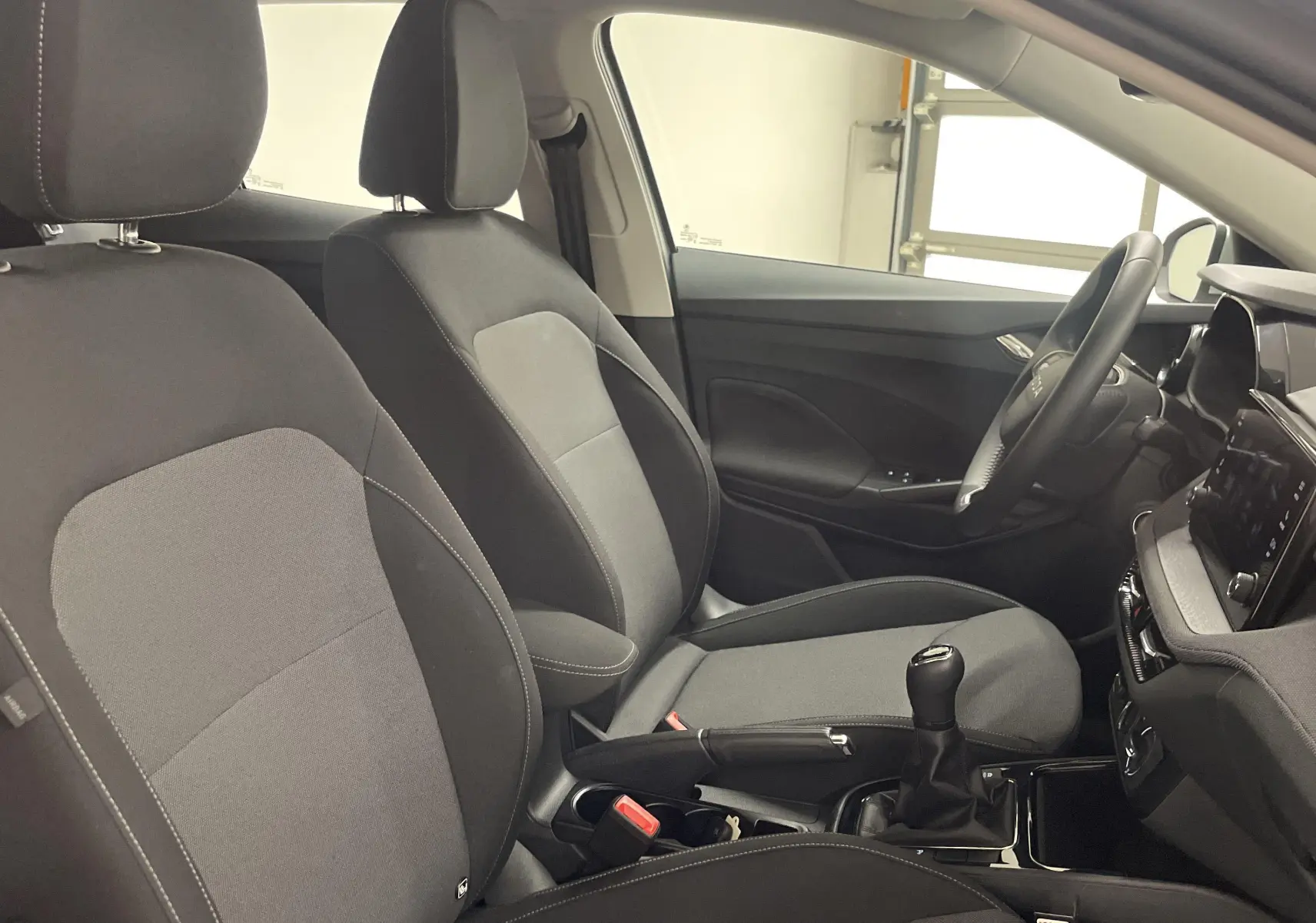 Vue intérieure côté conducteur de la Skoda Fabia 2025 avec sièges tissu gris et levier de vitesses manuel.