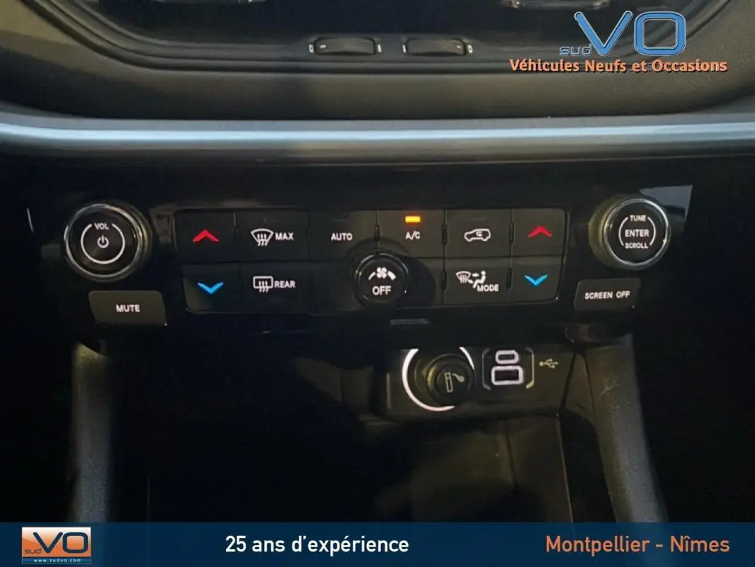 Plan rapproché du tableau de bord du Jeep Compass noir, mettant en valeur les commandes de climatisation et les prises USB.