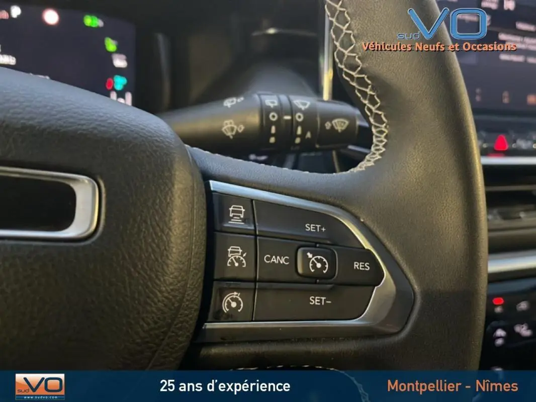 Gros plan sur les commandes du régulateur de vitesse au volant cuir du Jeep Compass noir, intérieur moderne et écran tactile visible.