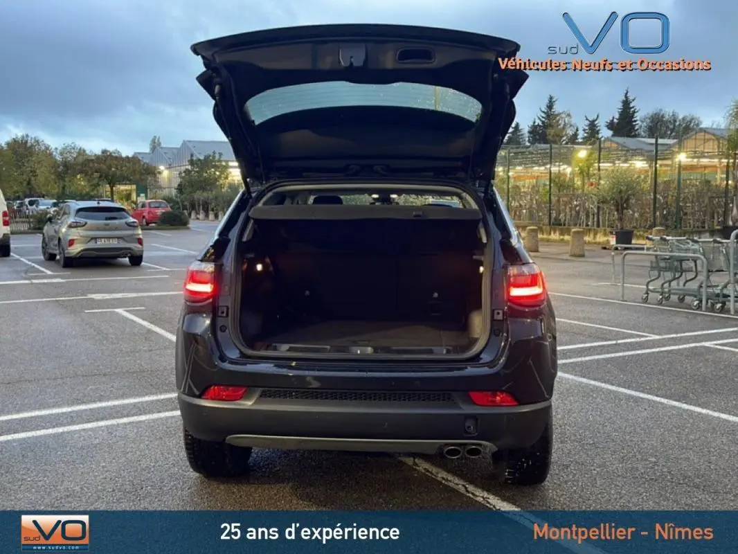 Vue arrière d'un Jeep Compass noir 2021 avec coffre ouvert et feux arrière allumés sur parking extérieur.