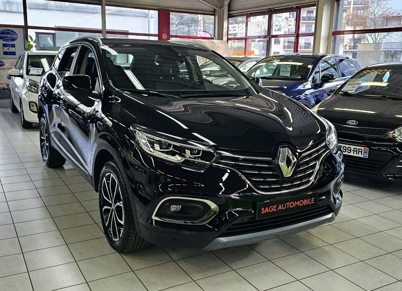 Renault Kadjar noir en 3/4 avant droit dans un showroom, avec jantes bi-ton et calandre chromée visible.
