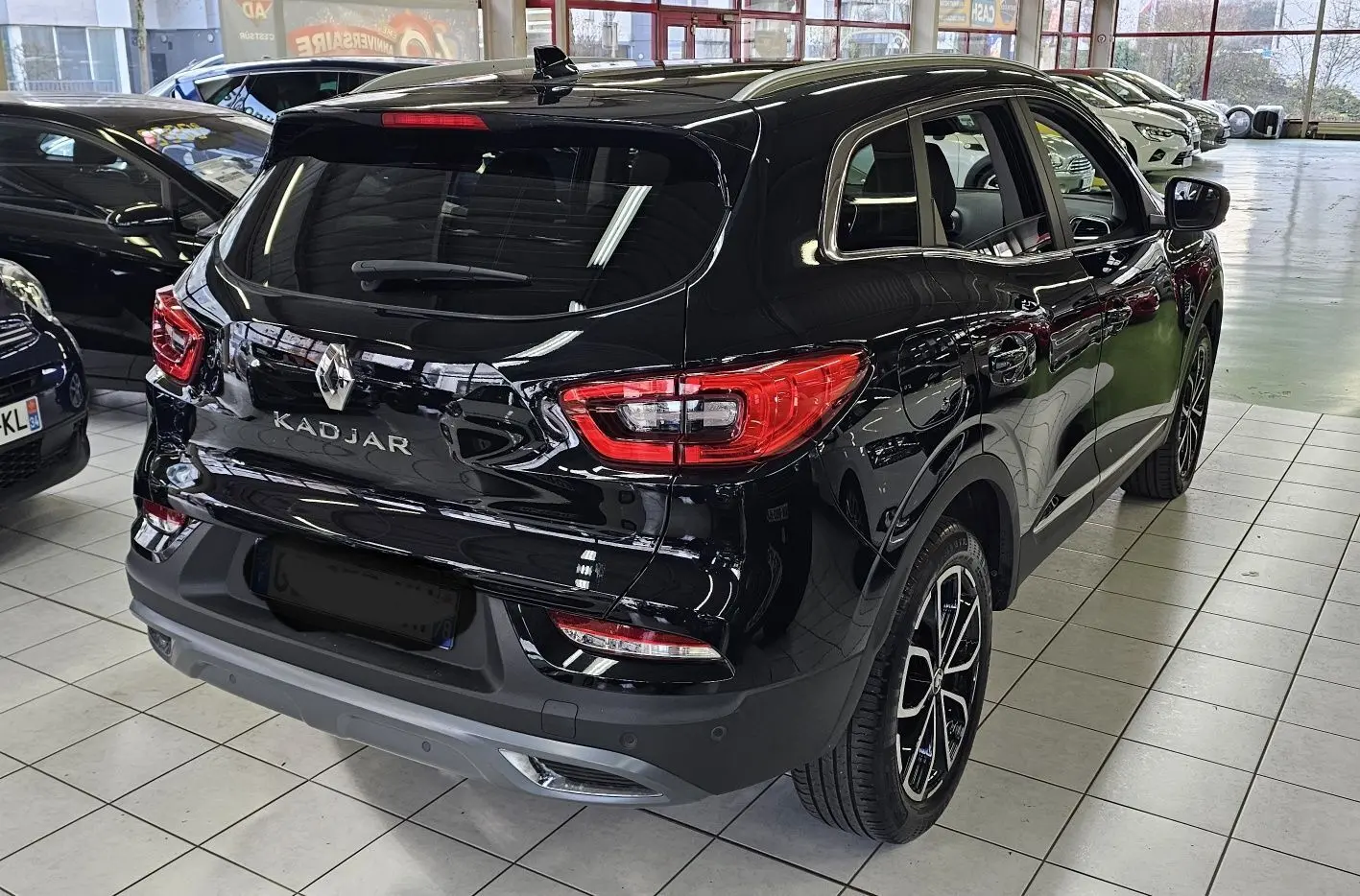Vue 3/4 arrière droite d'un Renault Kadjar noir brillant avec feux arrière LED et jantes bi-ton en showroom.