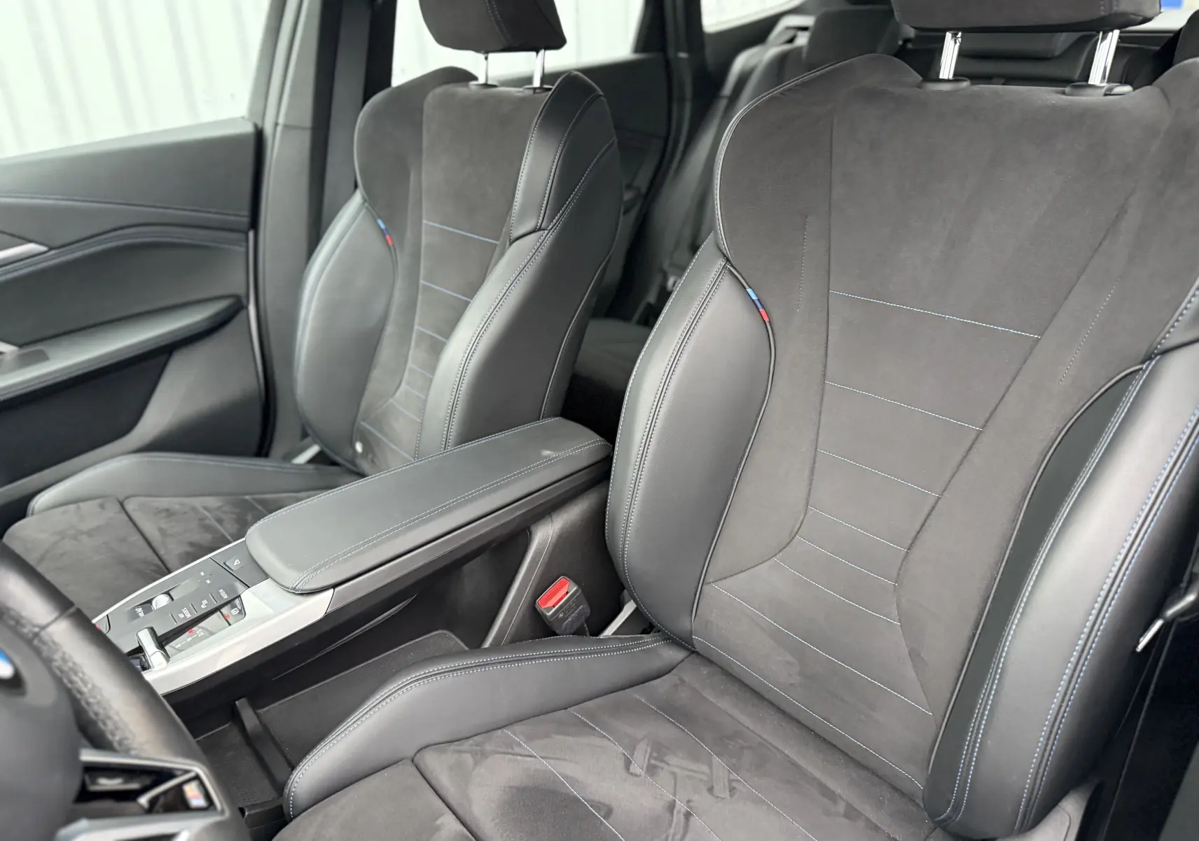 Vue intérieure avant du BMW X1 20D 2025 avec tableau de bord moderne, écran tactile et volant multifonction noir.