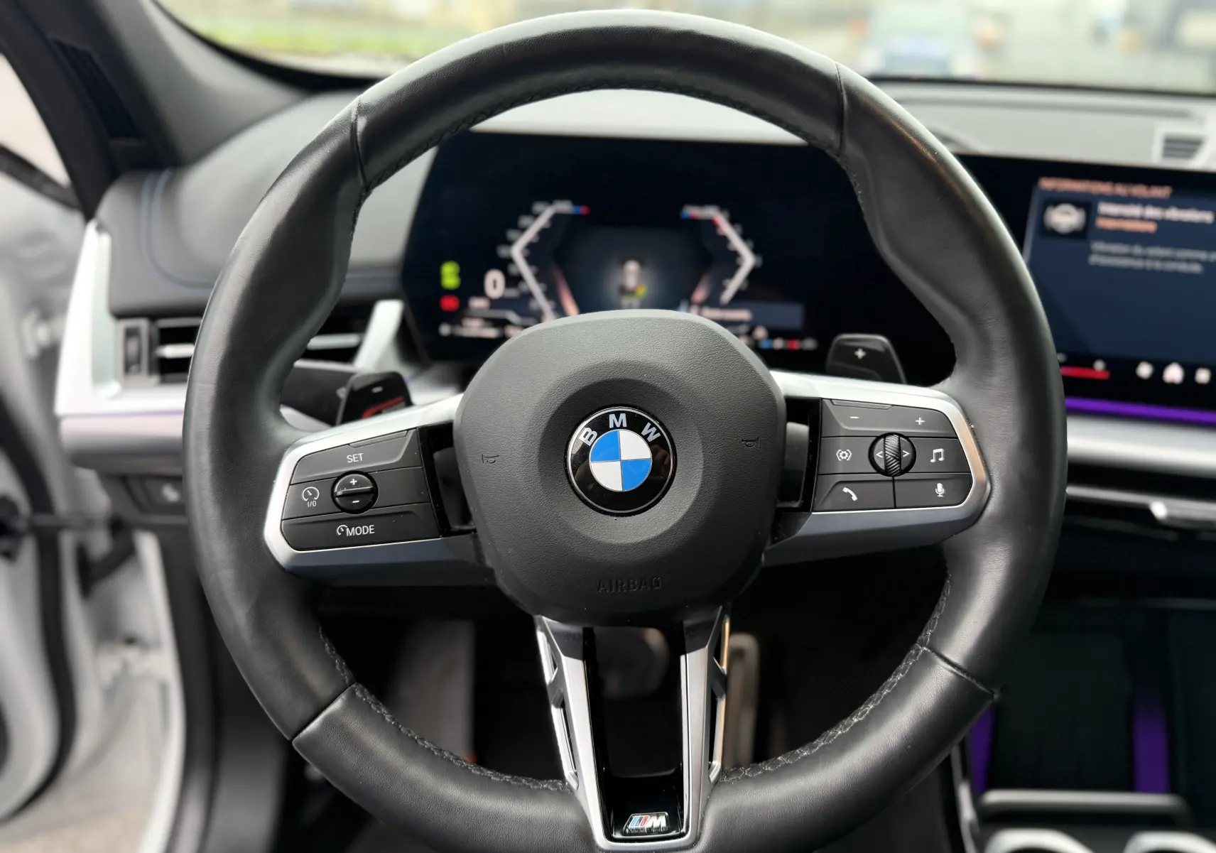 Gros plan sur le volant noir de la BMW X1 blanc minéral, mettant en valeur les commandes de régulateur de vitesse côté gauche.