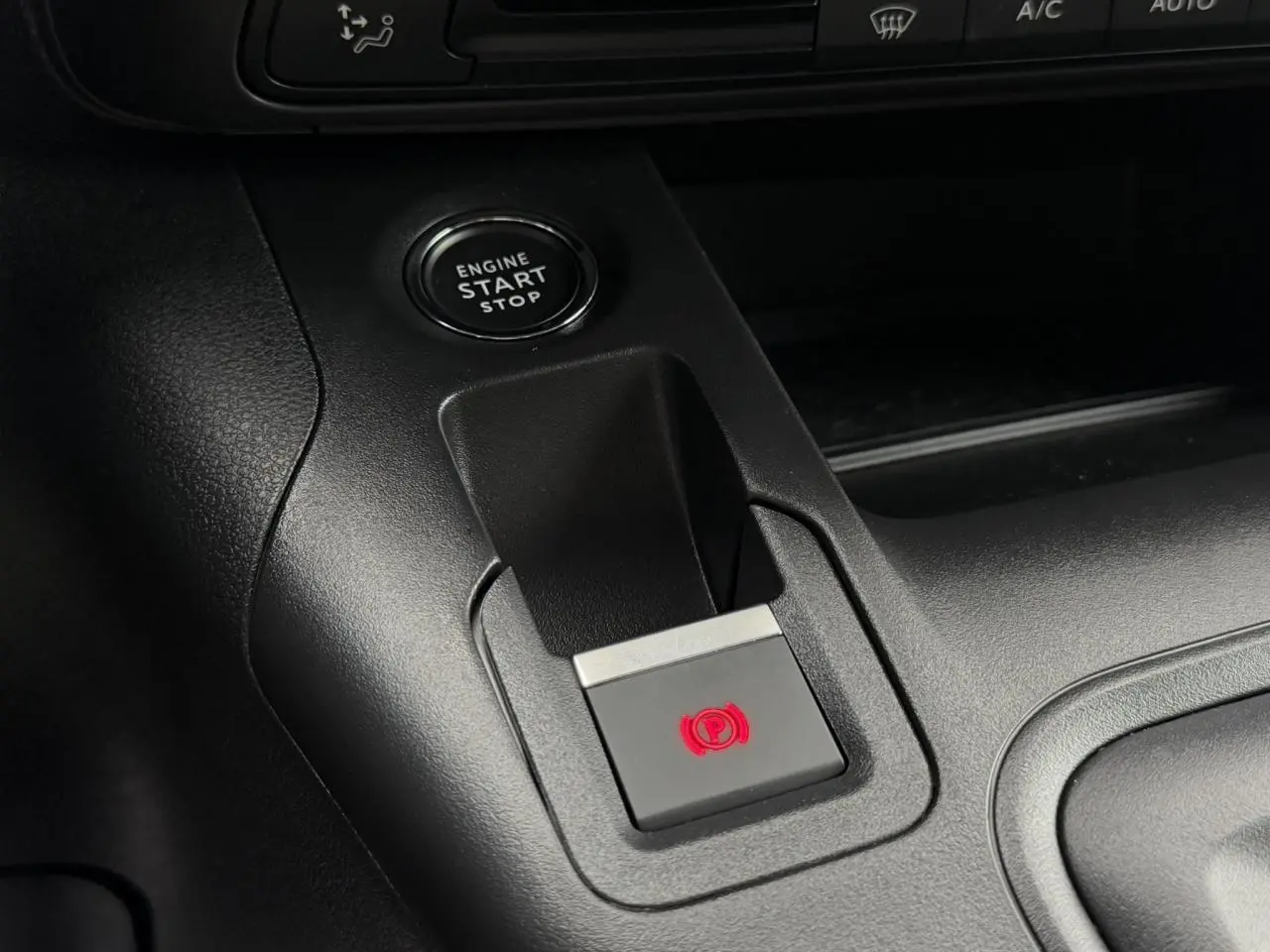 Gros plan sur la console centrale du Peugeot Rifter gris acier, montrant le bouton de frein de stationnement électrique et démarrage moteur.