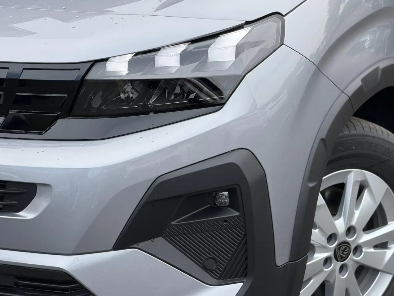 Gros plan sur l'avant droit du Peugeot Rifter gris acier, mettant en valeur le phare LED et la jante alu 16 pouces.
