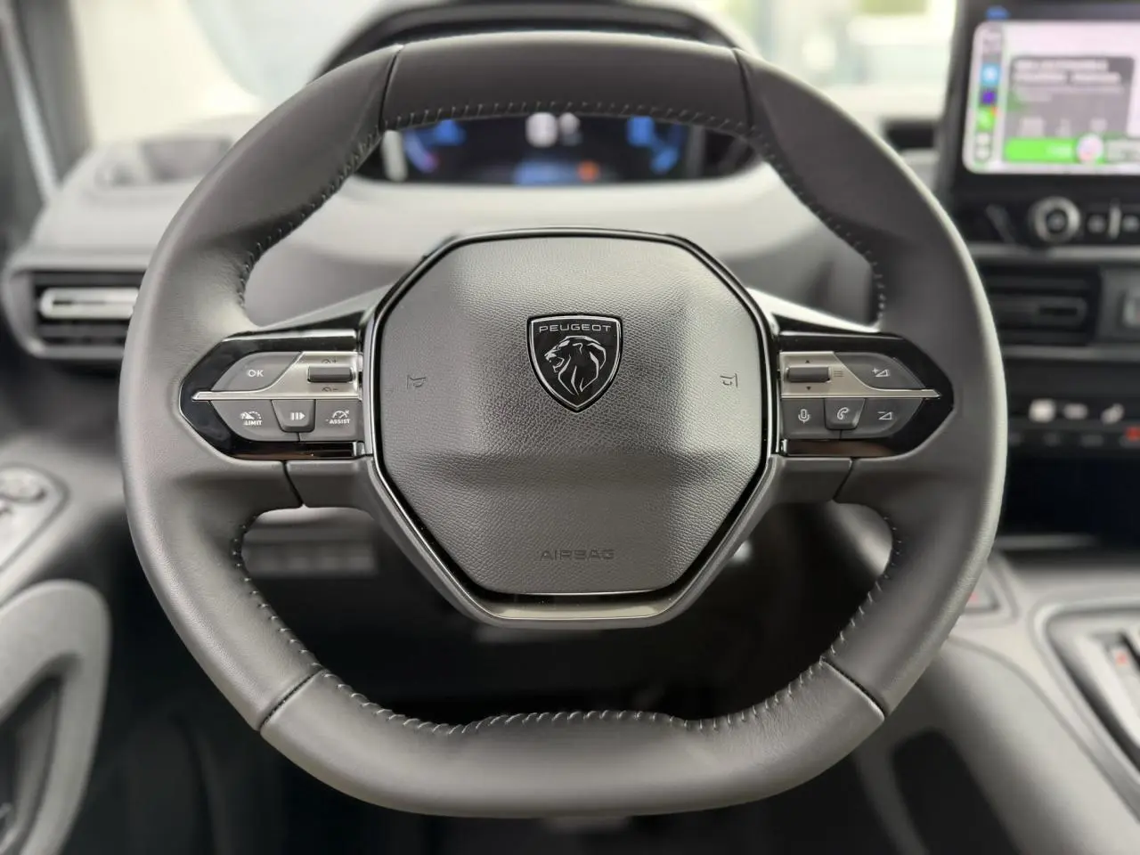 Volant cuir multifonction Peugeot Rifter vu de face avec commandes intégrées et tableau de bord flou en arrière-plan.