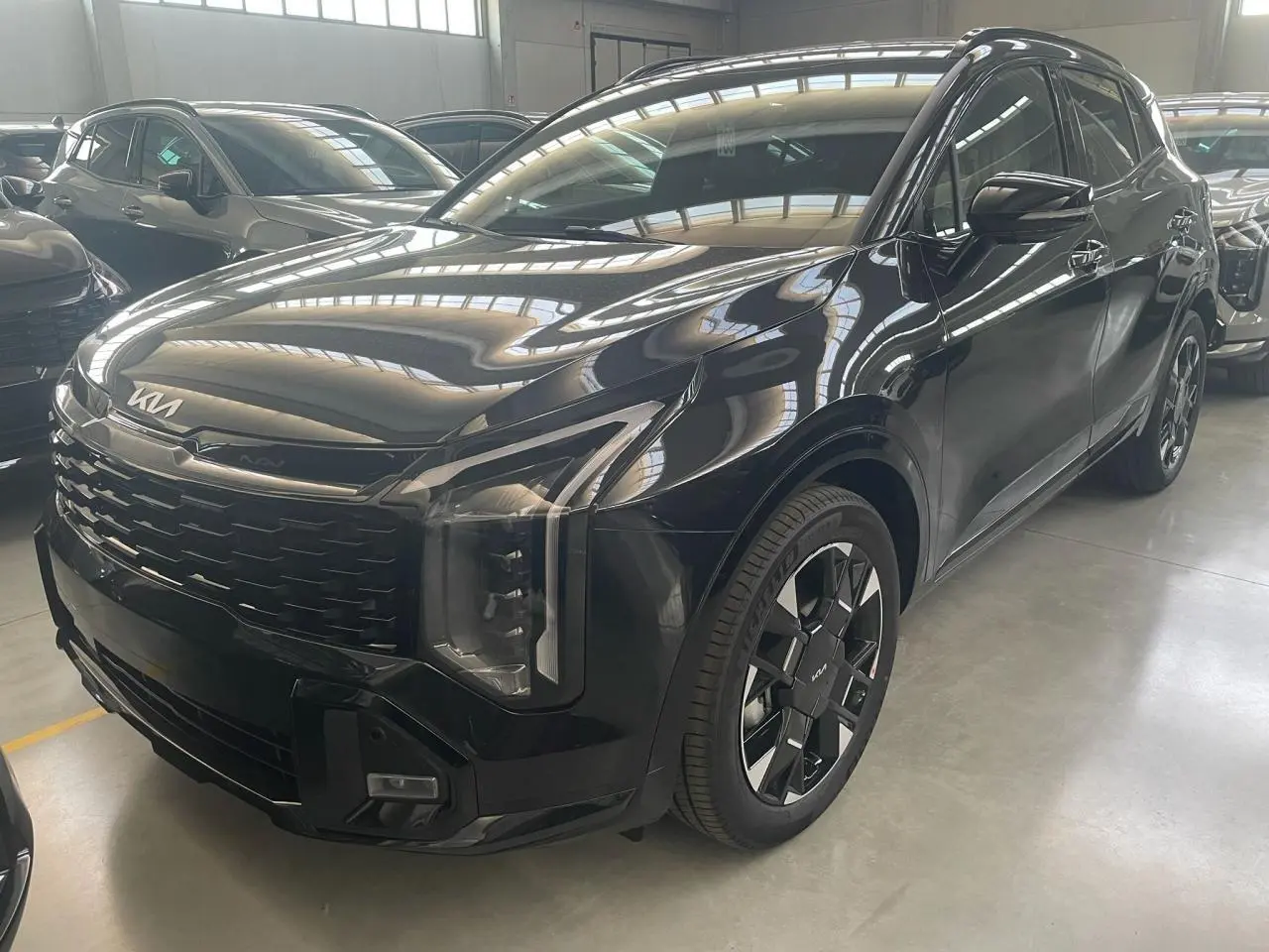 KIA Sportage Hybride noir vu en 3/4 avant droit, avec calandre imposante et jantes noires distinctives GT-Line.