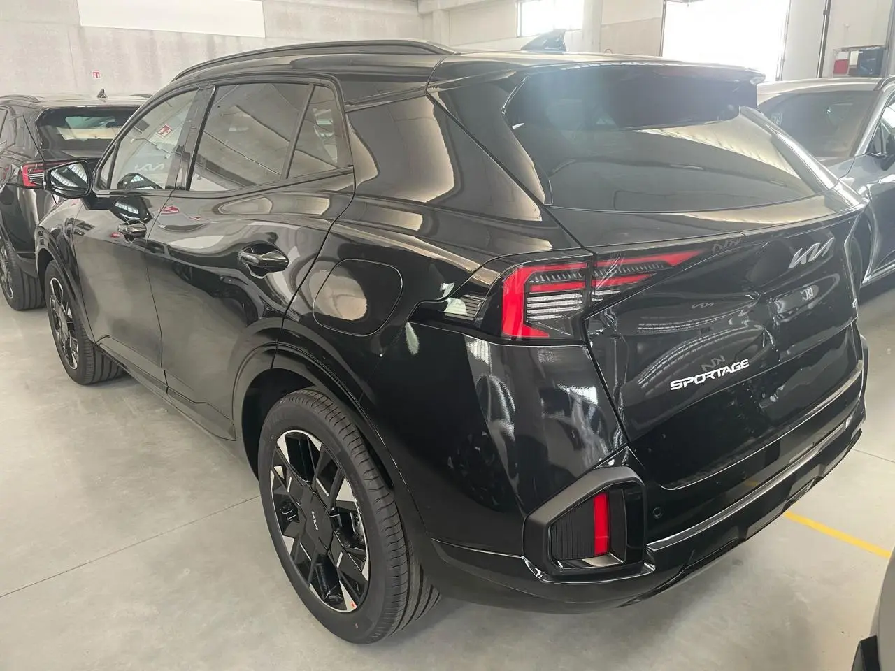 Vue 3/4 arrière droite du KIA SPORTAGE hybride noir 2026 avec feux arrière LED et jantes noires distinctives.