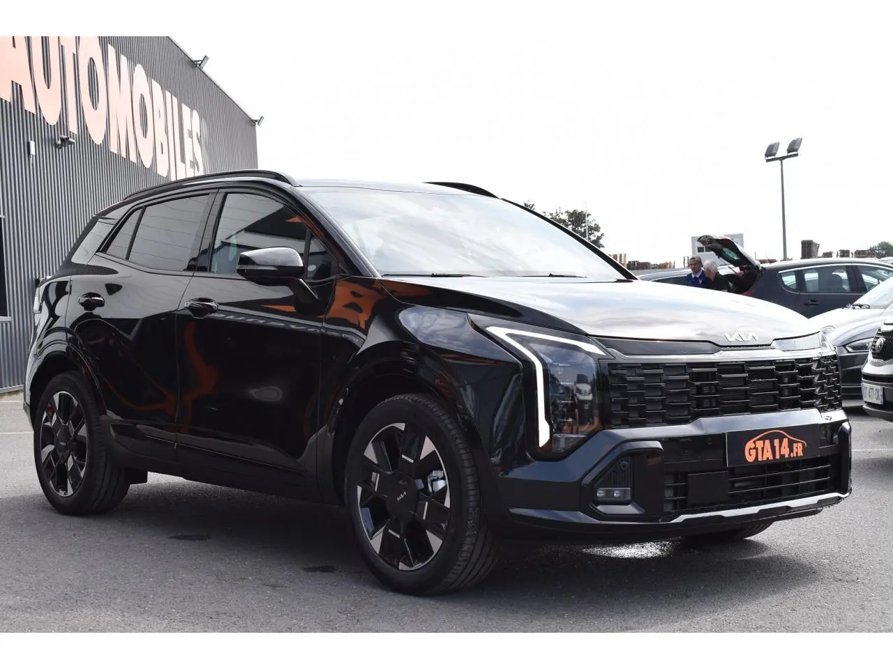 KIA Sportage hybride noir vu en 3/4 avant droit, avec calandre imposante et jantes 19 pouces noires.