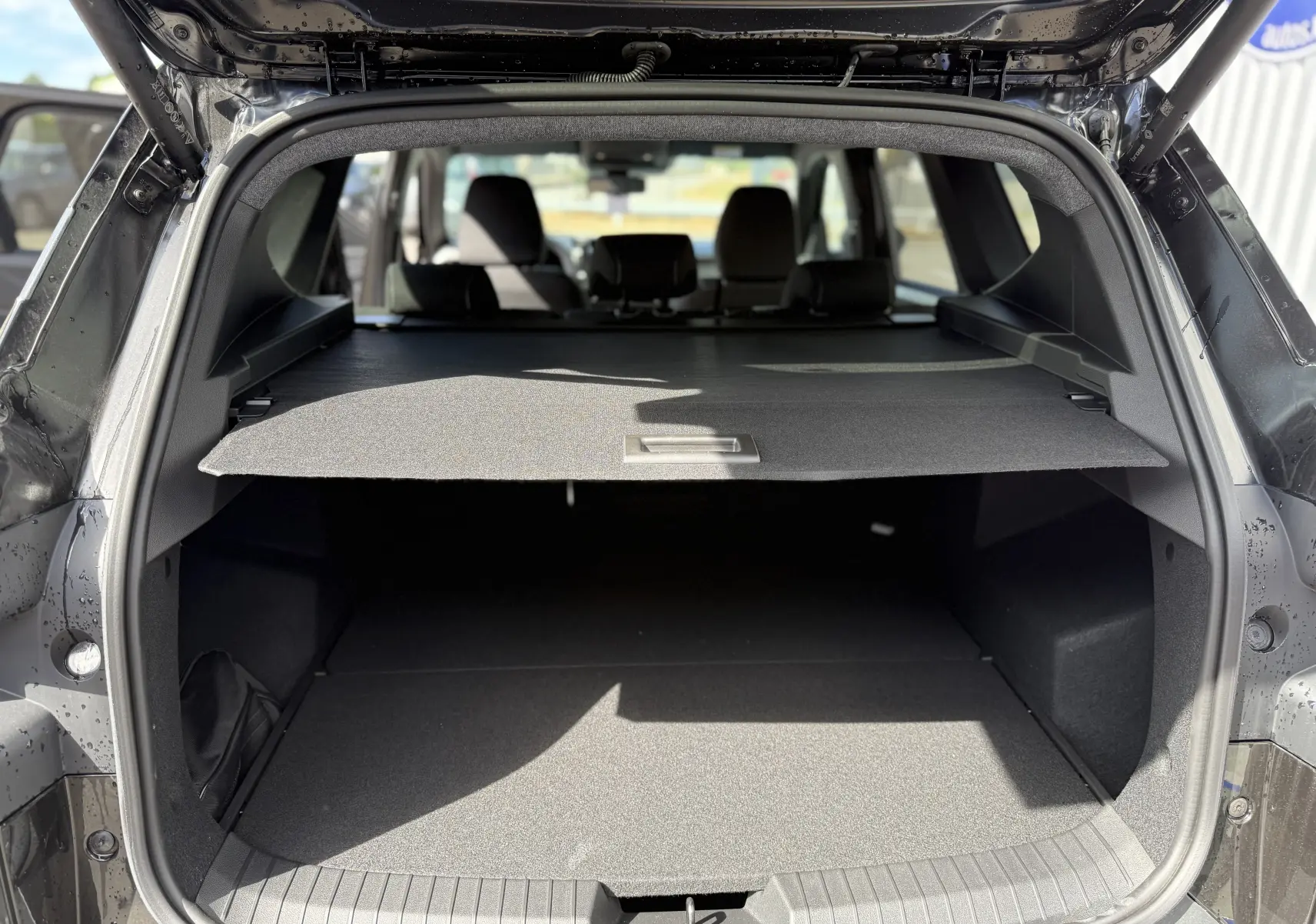 Vue arrière du coffre ouvert du Dacia Bigster noir nacré, montrant la plage arrière et l’espace de chargement.