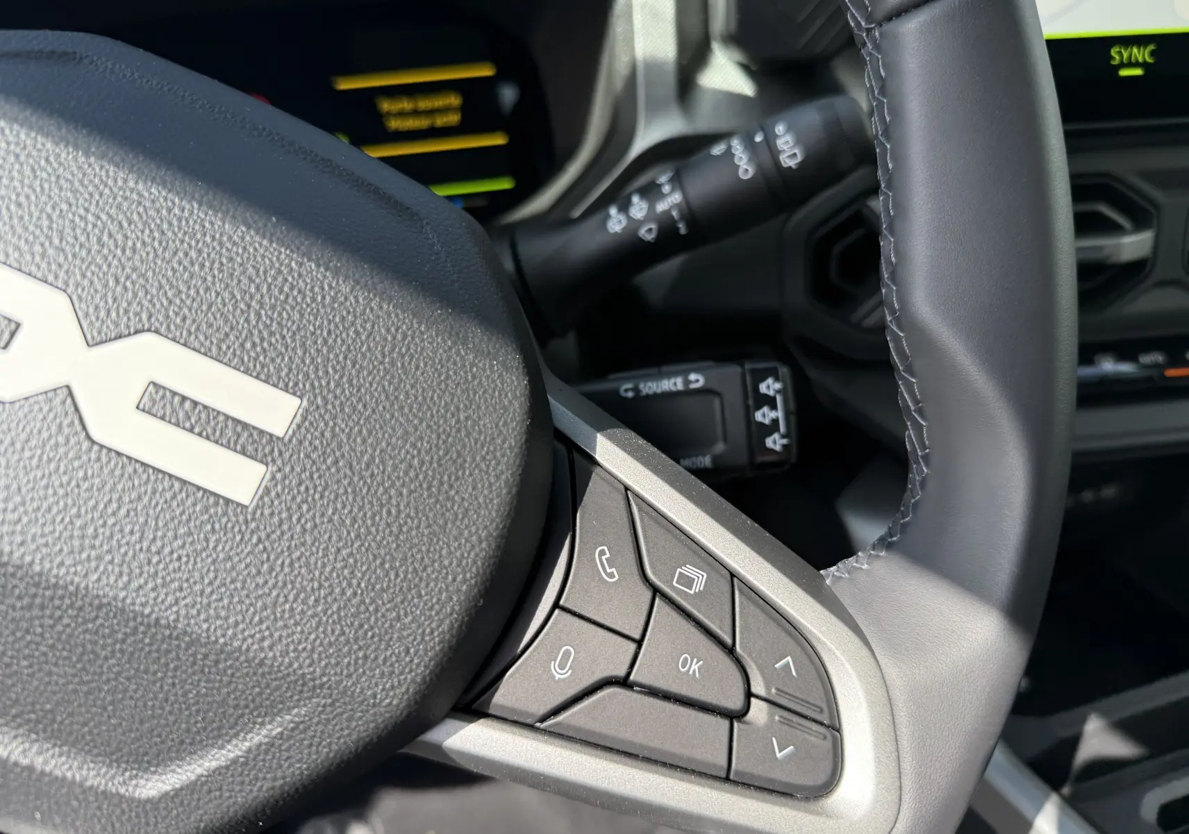 Gros plan sur le volant noir nacré du Dacia Bigster Hybrid 155 Journey, avec commandes intégrées et tableau de bord partiellement visible.