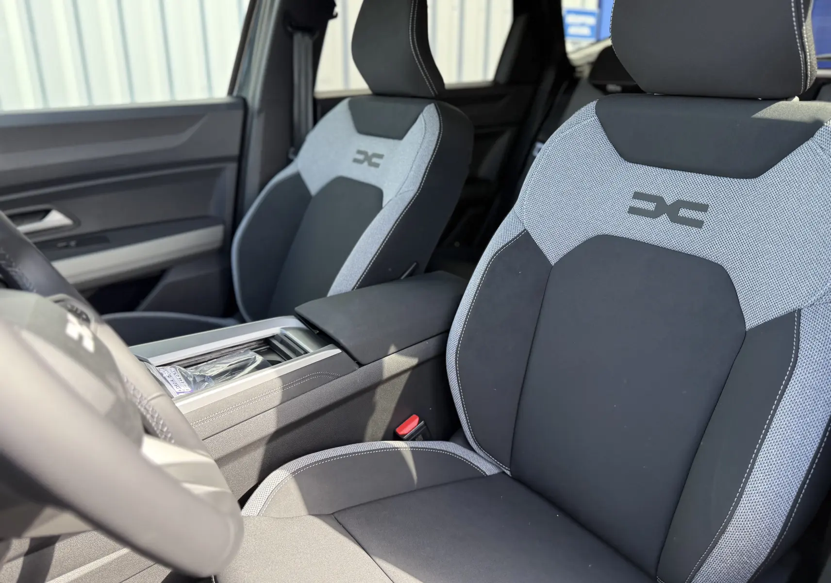 Vue intérieure rapprochée des sièges avant gris et noirs du Dacia Bigster Hybrid 155 Journey, avec logo distinctif brodé.