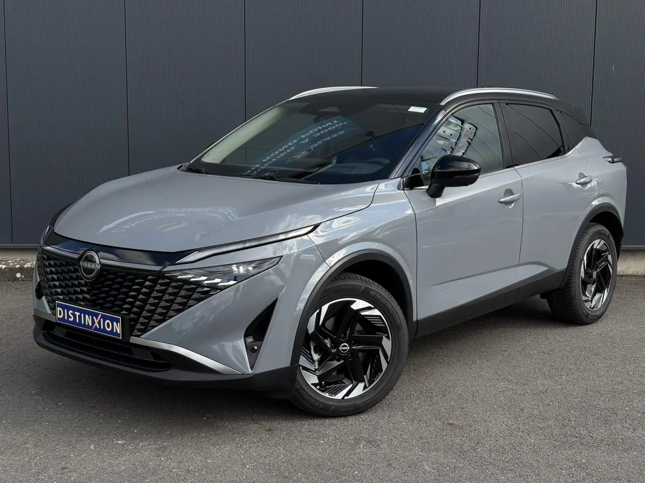 Nissan Qashqai gris Ceramic en 3/4 avant droit, avec calandre noire et jantes alliage noires distinctives.