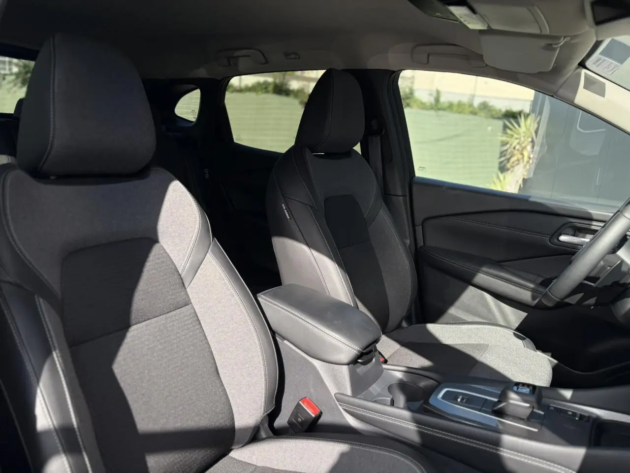 Intérieur du Nissan Qashqai 2025 montrant les sièges avant en tissu noir et gris avec accoudoir central et console.