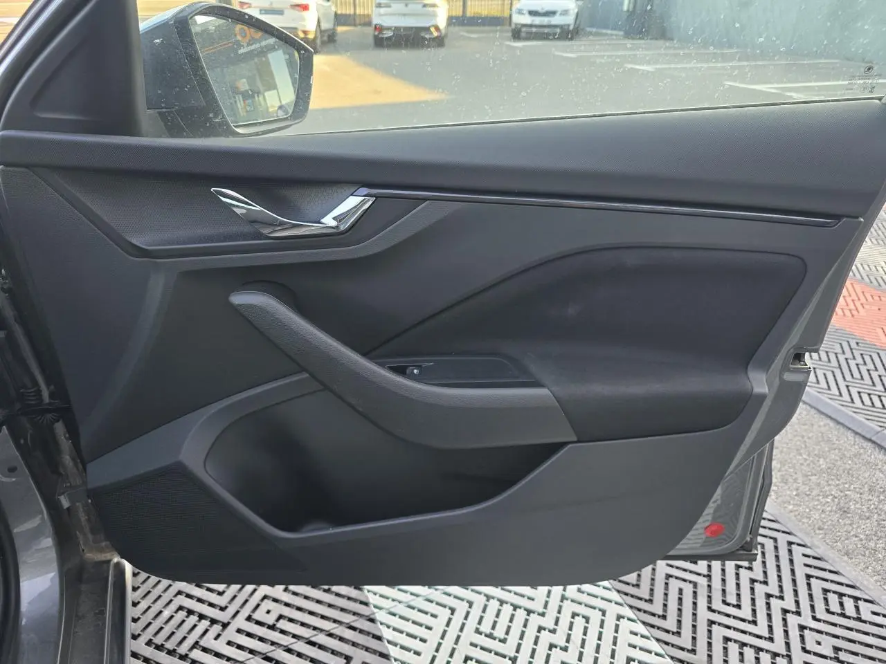 Vue intérieure de la porte avant gauche d'une Skoda Scala 2024 gris graphite, avec poignée chromée et commandes vitres.