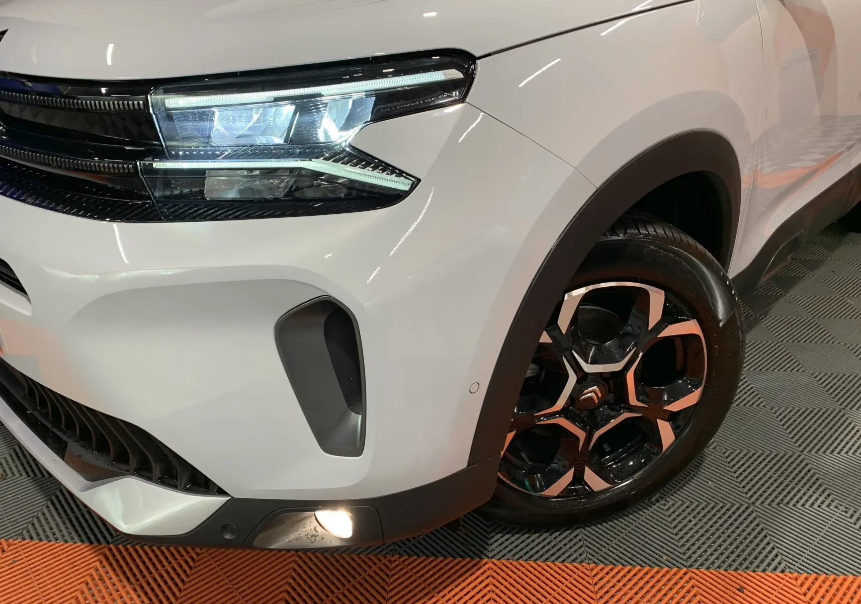 Gros plan sur l'avant droit blanc du Citroën C5 Aircross hybride 2024, mettant en valeur son phare LED et sa jante bi-ton.